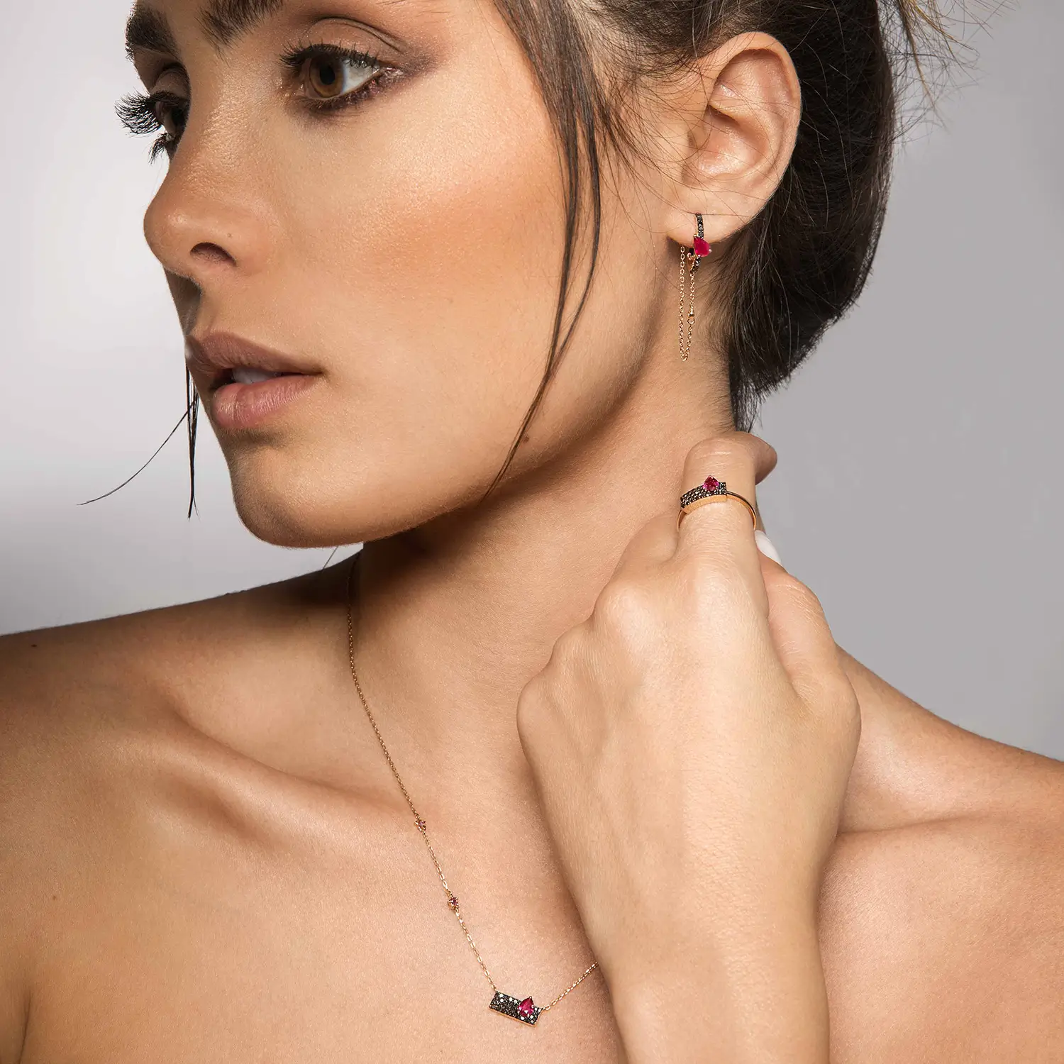 Model wearing 18kt rose gold ruby and black diamond jewelry set with necklace, earrings, and ring